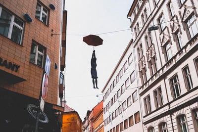 During the day, a woman in between buildings umbrellas when suspended on the wire
